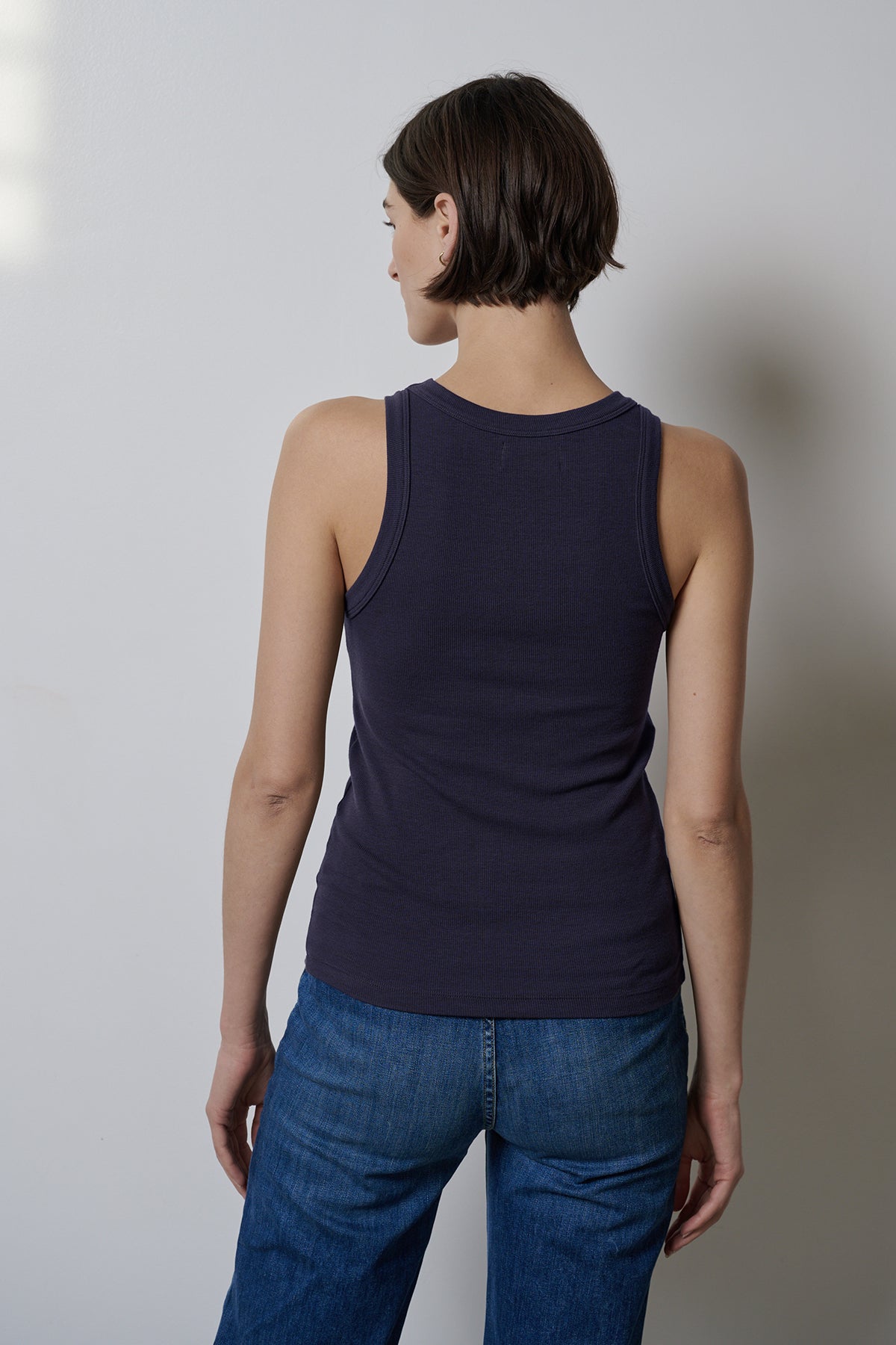 The woman's back view showcases a form-fitting CRUZ tank top by Velvet by Jenny Graham paired with jeans that offer stretch for comfort.-35547435008193