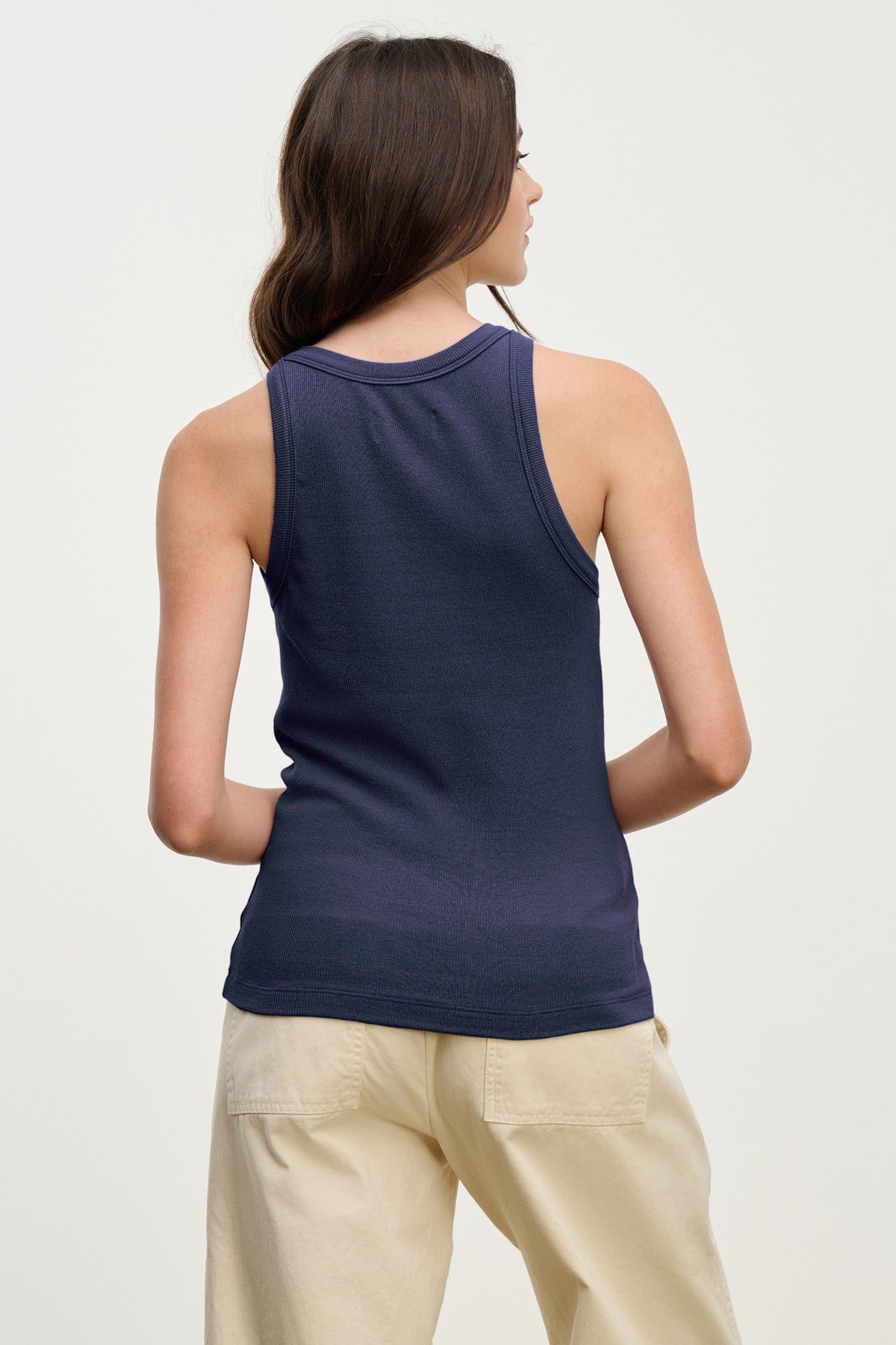 A person with long brown hair is seen from the back, wearing the Velvet by Jenny Graham CRUZ TANK TOP in navy blue and light beige pants against a plain light background—classic pieces for any capsule wardrobe.-41629728276673