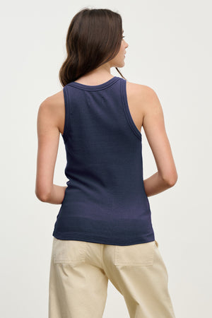 A person with long brown hair is seen from the back, wearing the Velvet by Jenny Graham CRUZ TANK TOP in navy blue and light beige pants against a plain light background—classic pieces for any capsule wardrobe.