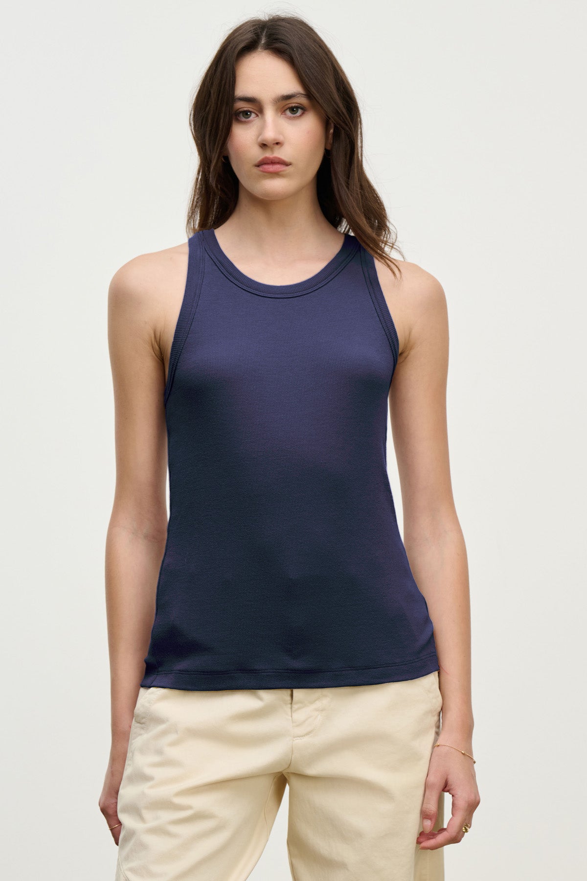 A woman in the CRUZ TANK TOP by Velvet by Jenny Graham, a sleeveless ribbed navy top styled with beige pants, stands against a plain light background, looking directly at the camera—perfect for a capsule wardrobe.