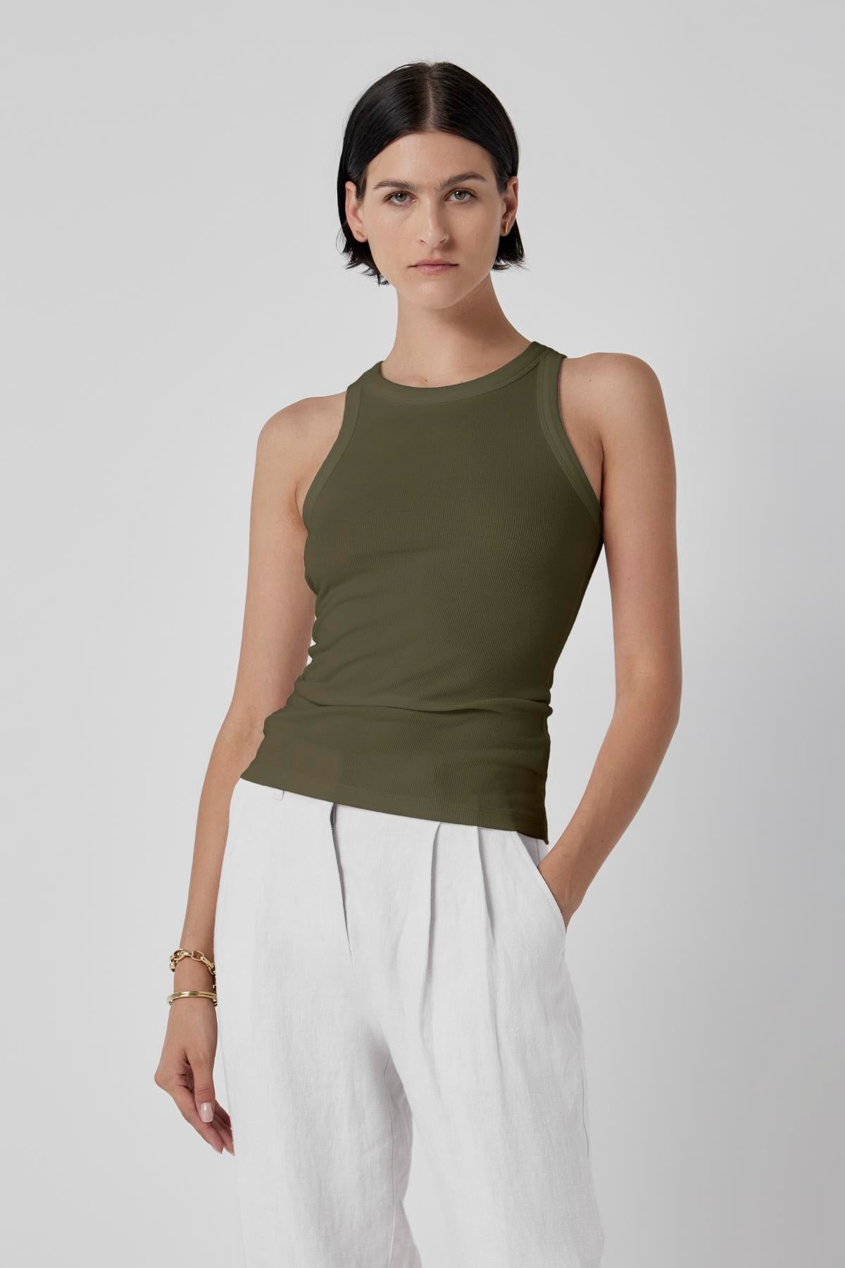   A person with short dark hair is wearing a sleeveless olive green CRUZ TANK TOP by Velvet by Jenny Graham and white pants, standing against a plain background. 