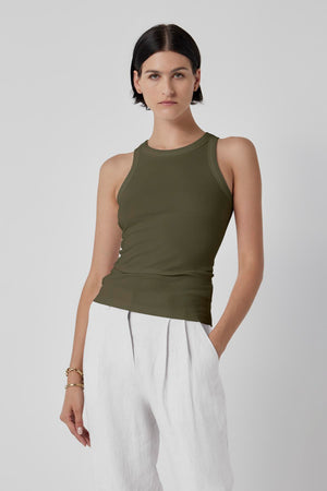 A person with short dark hair is wearing a sleeveless olive green CRUZ TANK TOP by Velvet by Jenny Graham and white pants, standing against a plain background.