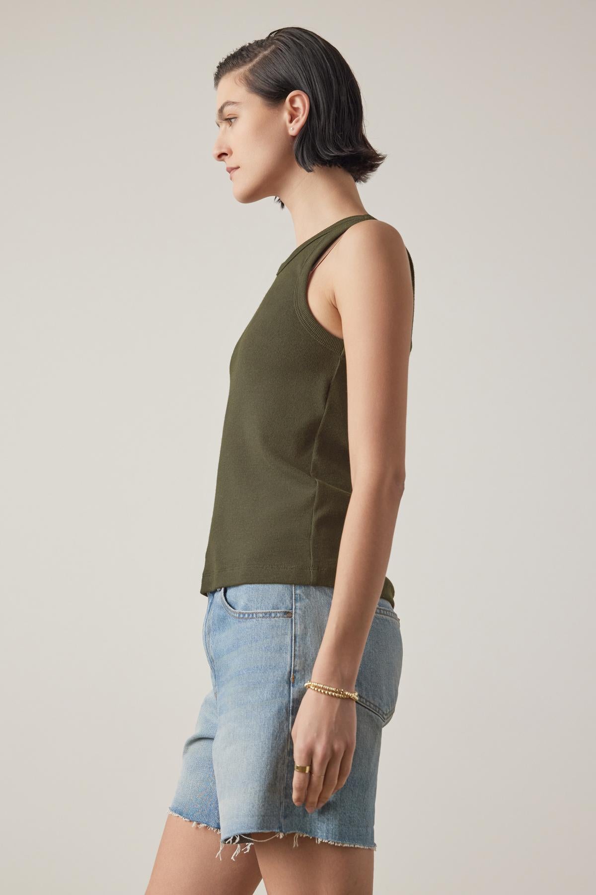   A person with short dark hair, wearing the Velvet by Jenny Graham CRUZ TANK TOP crafted from a ribbed cotton-modal blend and denim shorts, is standing in profile against a plain background. 