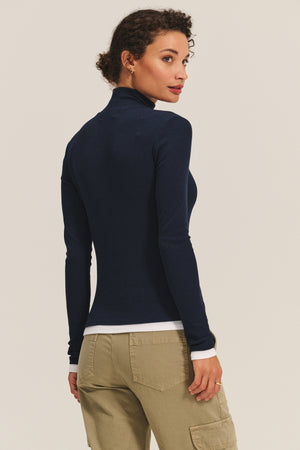 A woman faces away, wearing the Velvet by Graham & Spencer LINDEN TEE in navy stretch modal rib with long sleeves, paired with light khaki cargo pants against a plain background.