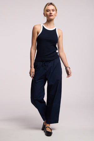 A person wears the LINDY TANK TOP by Velvet by Graham & Spencer—a black and white ribbed, fitted tank—paired with navy wide-leg pants and black shoes, standing against a plain light background.