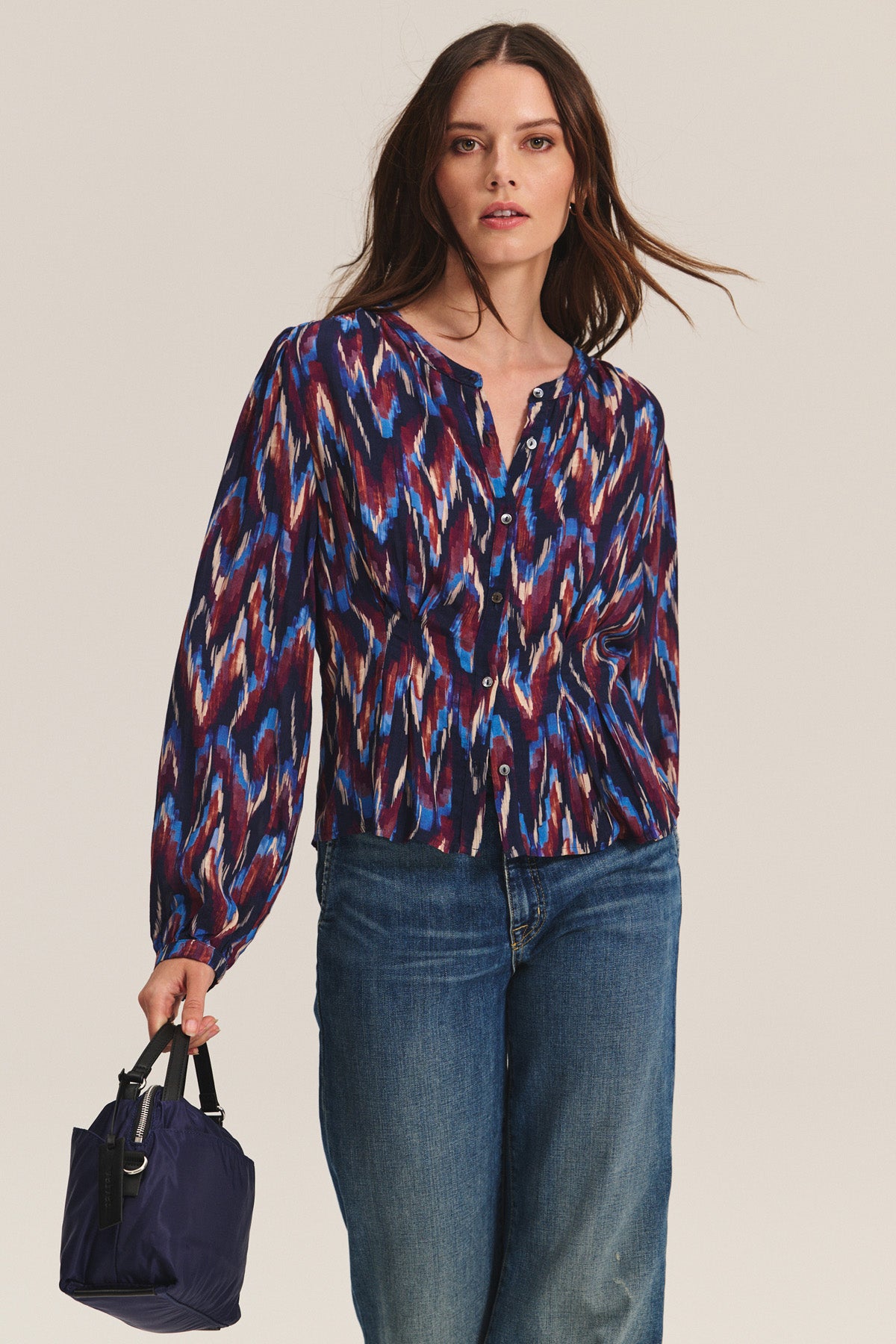 A woman models the ESTELLA BLOUSE by Velvet by Graham & Spencer—a multicolored, long-sleeve cotton-viscose top—paired with blue jeans and a small navy handbag against a plain background.