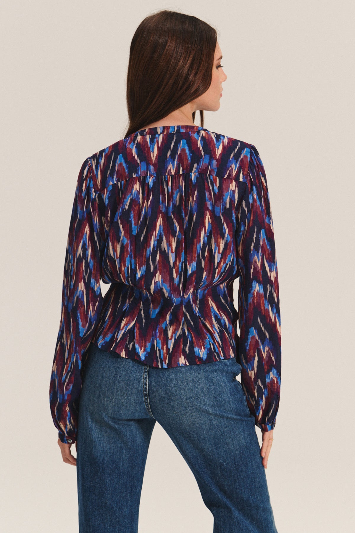 A woman is seen from the back in the ESTELLA BLOUSE by Velvet by Graham & Spencer—a long-sleeve, multicolored cotton-viscose top—paired with blue jeans against a plain background, highlighting its versatile style.-40732534374593