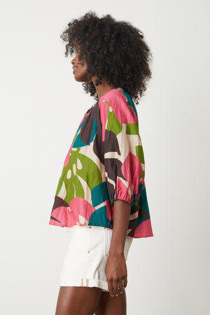 the back view of a woman wearing a Velvet by Graham & Spencer ARIEL PRINTED TOP brightly colored Monstera leaf print and white denim shorts side view.