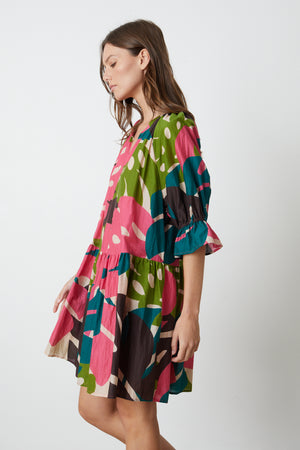 A woman wearing a Velvet by Graham & Spencer Tracy Printed Dress in bold colored Monstera print side view
