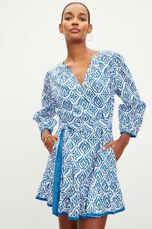 The model is wearing a blue and white KENLEY PRINTED BOHO DRESS made of cotton by Velvet by Graham & Spencer.