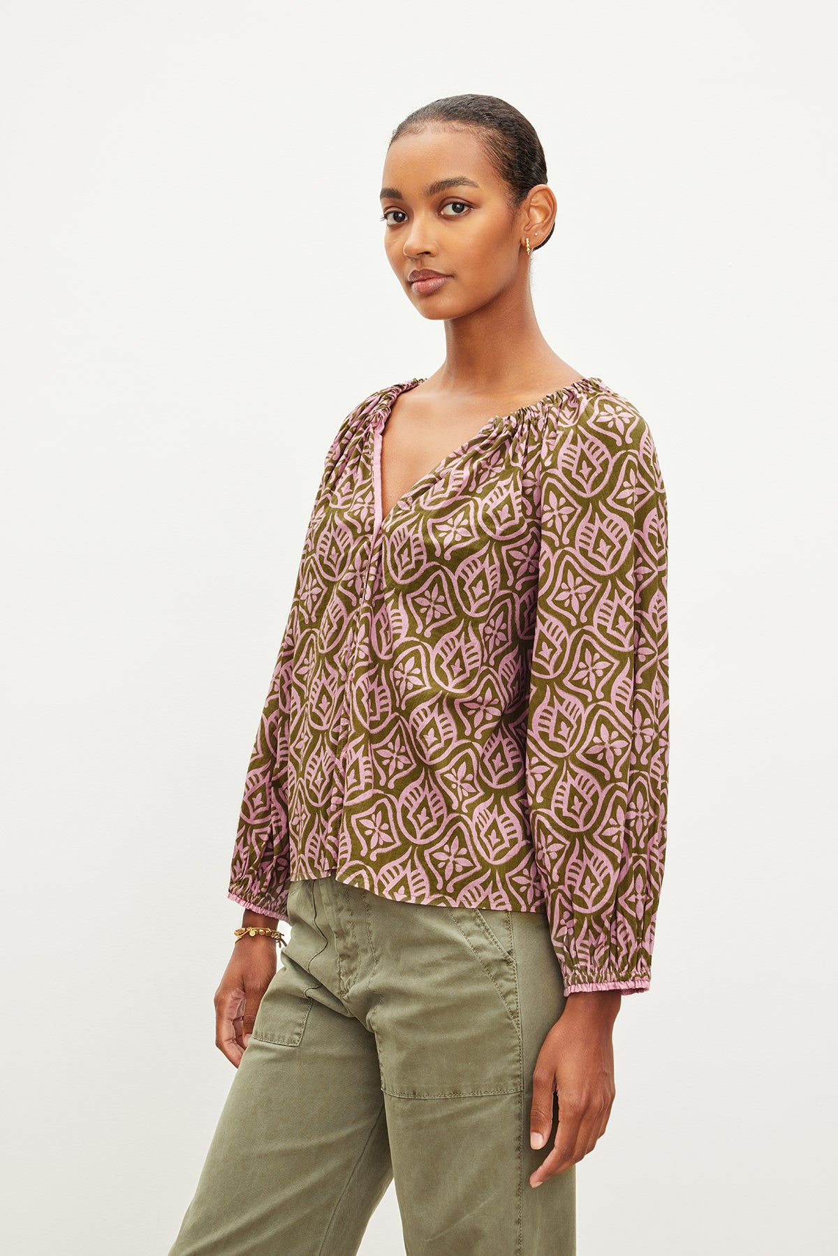   The model is wearing an MARIAN PRINTED BUTTON FRONT TOP by Velvet by Graham & Spencer, an olive green top with a v-neckline. 