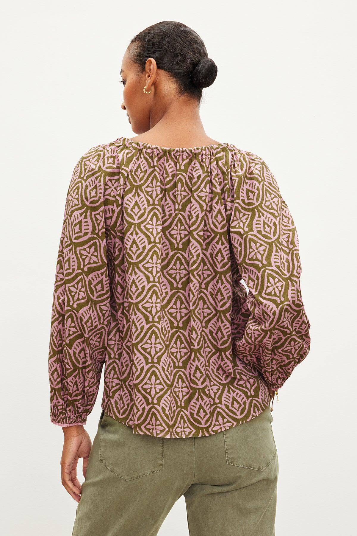   The back view of a woman wearing the Velvet by Graham & Spencer MARIAN PRINTED BUTTON FRONT TOP with a geometric pattern. The blouse features a v-neckline and is made of mosaic printed cotton, with the buttoned front adding an extra touch. 