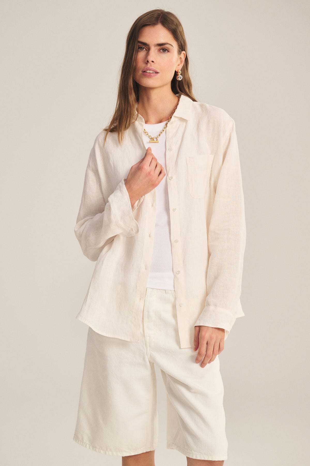 A woman wears the MULHOLLAND LINEN SHIRT by Velvet by Jenny Graham, styled with a white top and knee-length shorts, standing against a plain background.-41044038713537