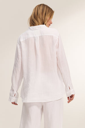 A woman faces away in the MULHOLLAND LINEN SHIRT by Velvet by Jenny Graham, styled with matching white pants against a neutral background.