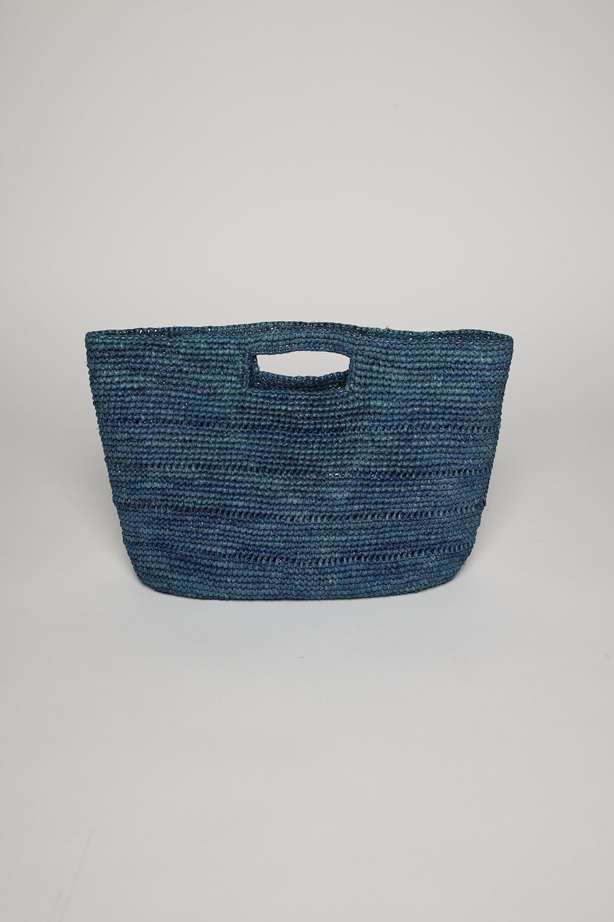 A blue Velvet by Graham & Spencer raffia straw basket with curved sides and an integrated handle, displayed against a white background.-36571449491649