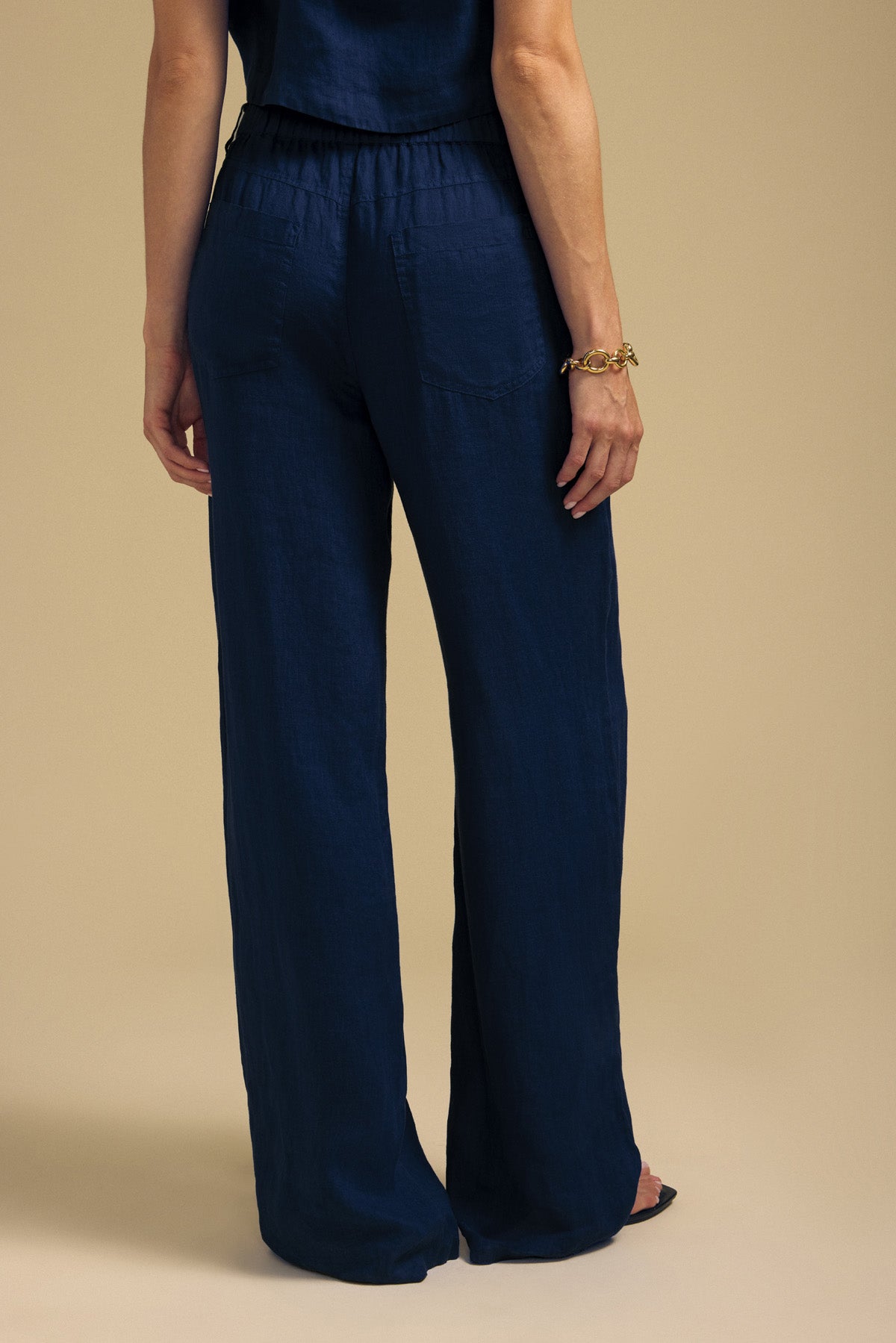 Back view of a person wearing dark blue NATALIE LINEN PANT wide-leg pants with an elastic waistband and a matching top.-46422215557313