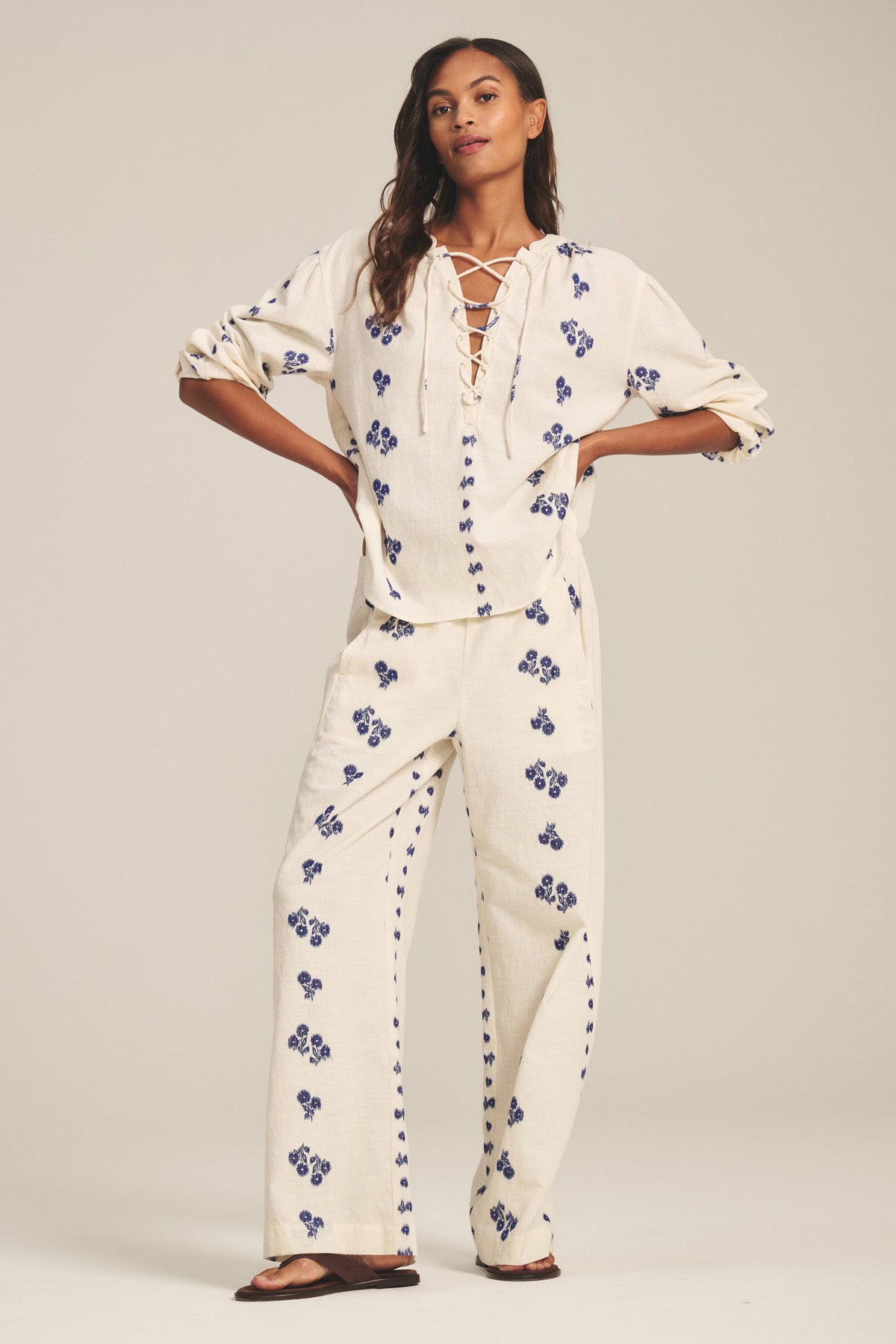 A woman models the Velvet by Graham & Spencer WINSLET TOP, a cream cotton jacquard piece with a relaxed boxy fit and blue floral pattern, paired with matching wide-leg pants and sandals against a plain backdrop.-41338483278017