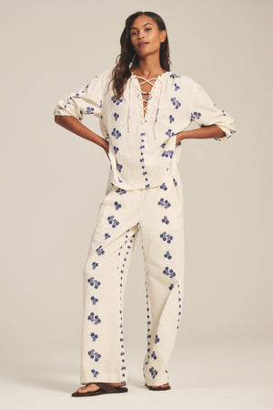 A woman models the Velvet by Graham & Spencer WINSLET TOP, a cream cotton jacquard piece with a relaxed boxy fit and blue floral pattern, paired with matching wide-leg pants and sandals against a plain backdrop.