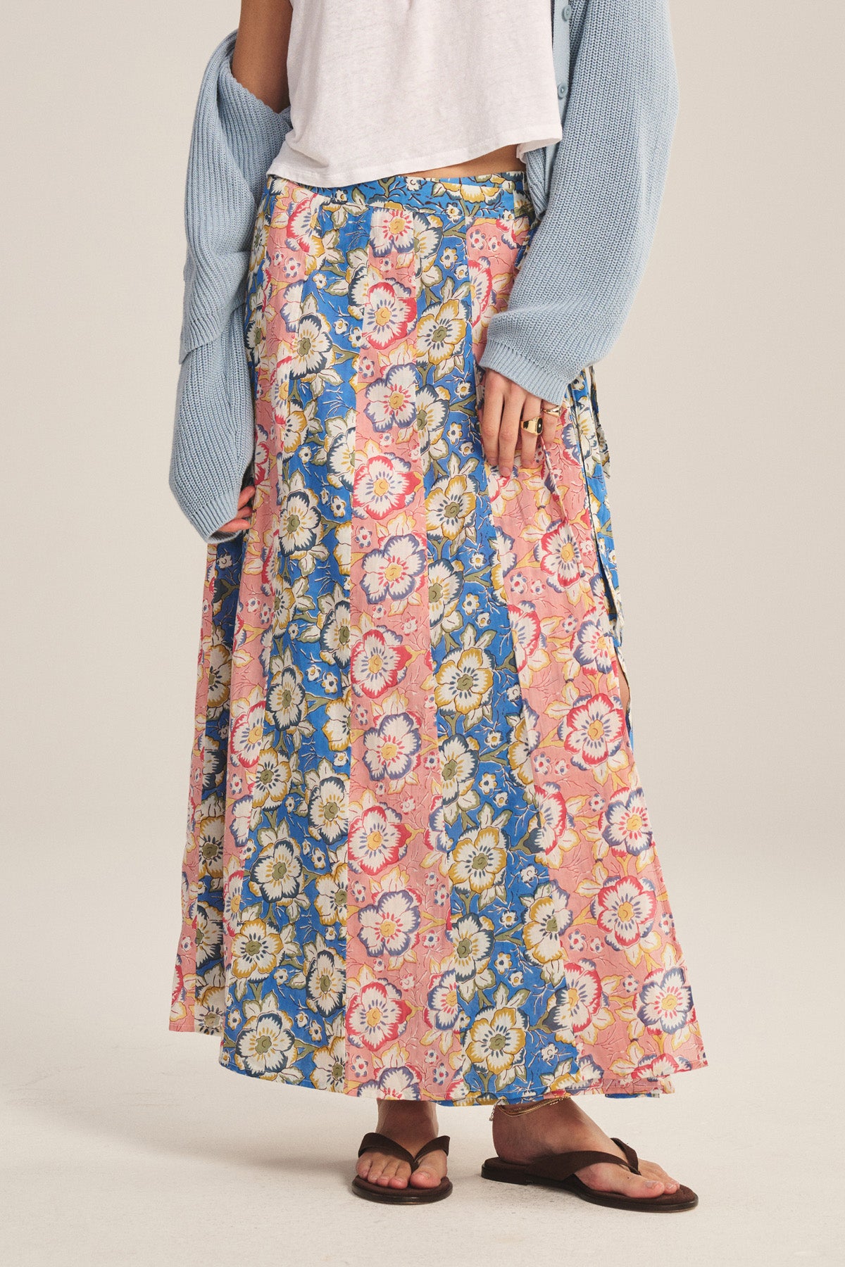 A person in the Velvet by Graham & Spencer NICOLETTE SKIRT with floral blue and pink panels, styled with a white top, light blue cardigan, and brown sandals.-41008375857345