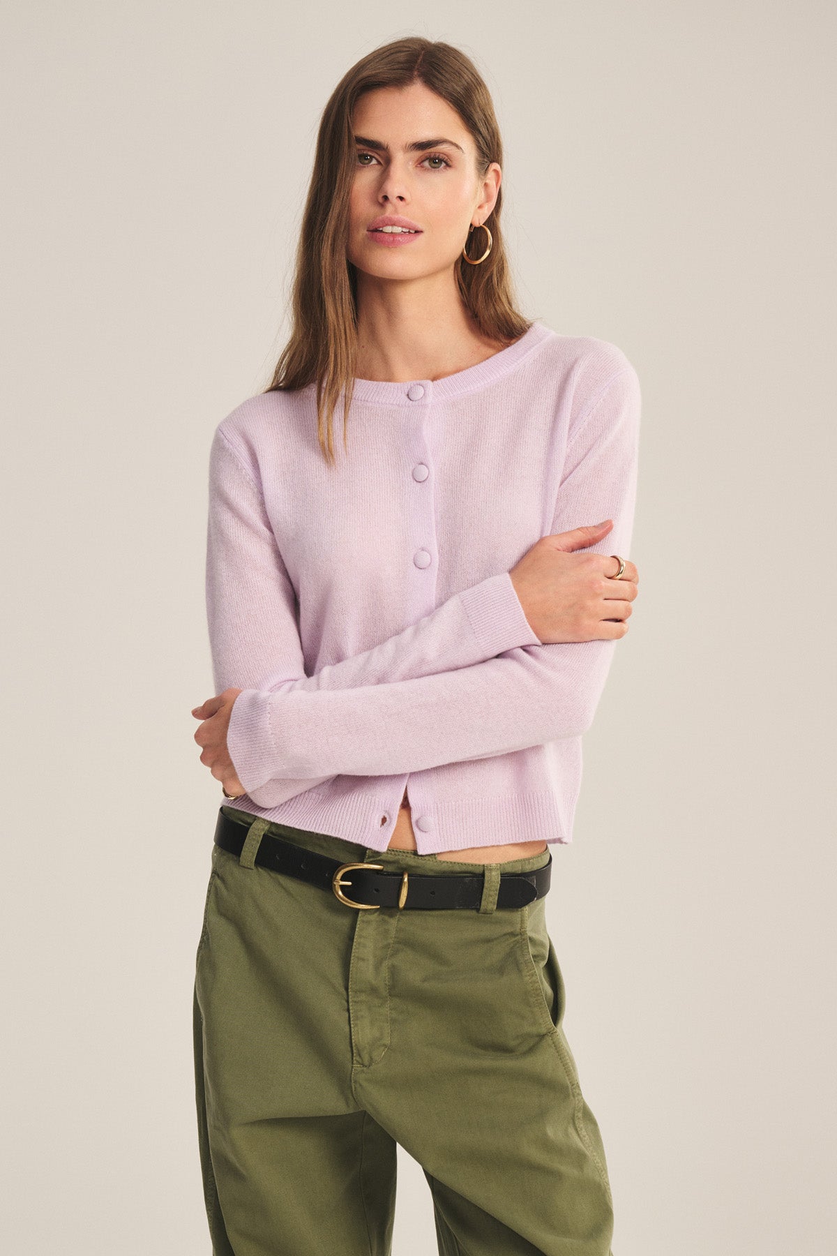 A person stands with arms crossed against a plain background, wearing the NOLIE CASHMERE CARDIGAN by Velvet by Graham & Spencer in light purple and olive green pants.