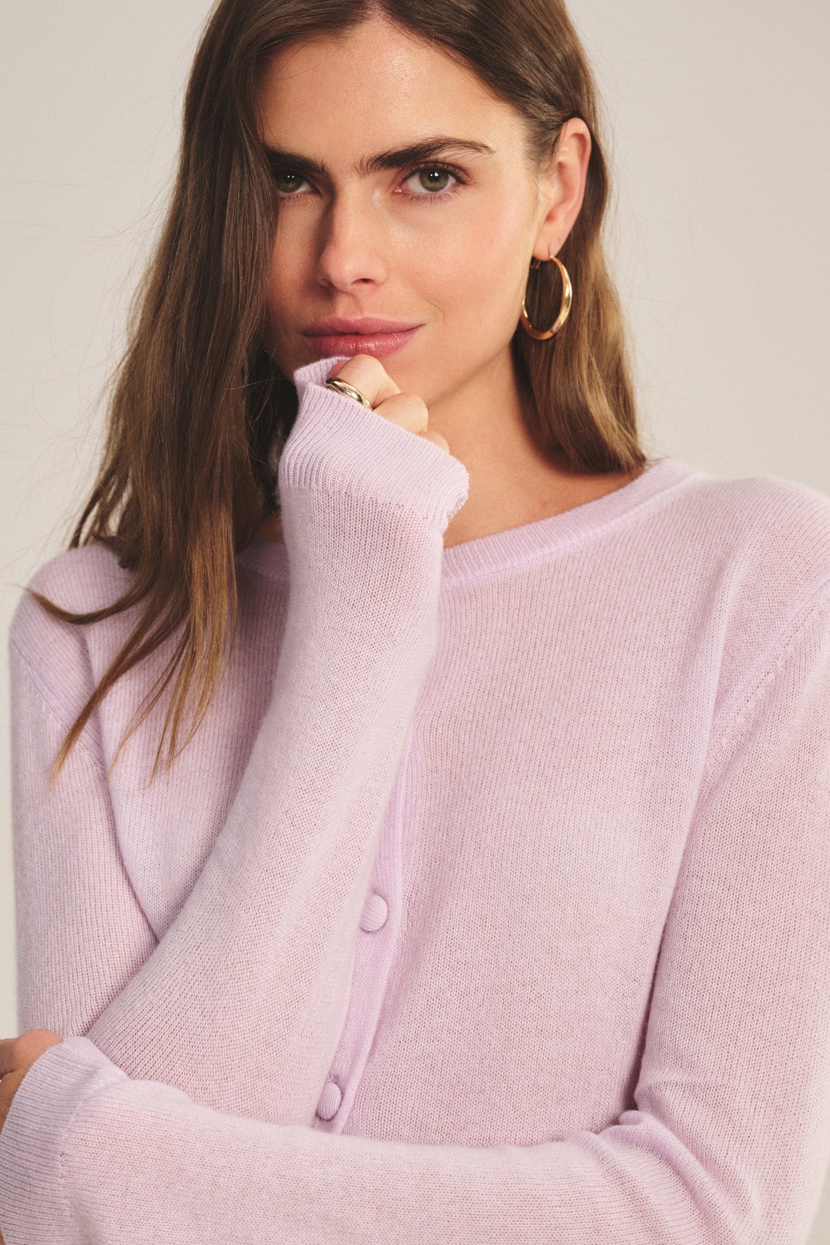 A woman wearing the NOLIE CASHMERE CARDIGAN by Velvet by Graham & Spencer, paired with gold hoop earrings and a ring, poses with her hand partially covering her mouth.-40808678981825
