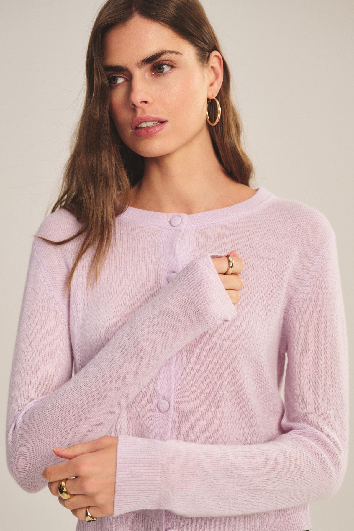 A woman wears the Velvet by Graham & Spencer NOLIE CASHMERE CARDIGAN in light pink with gold hoop earrings, standing against a plain background.