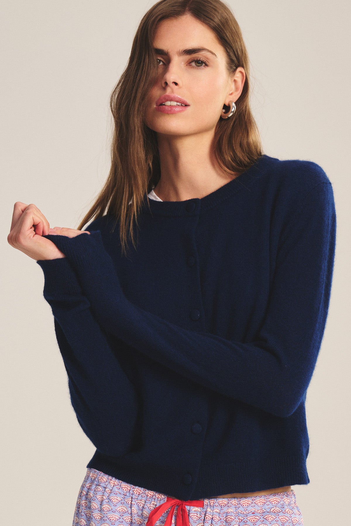 A woman wearing the NOLIE CASHMERE CARDIGAN by Velvet by Graham & Spencer in navy blue, paired with patterned pants, stands against a plain background.