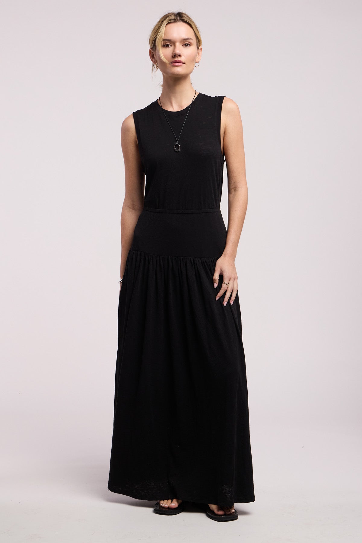A woman faces forward wearing the LUNETTA DRESS by Velvet by Graham & Spencer, styled with black sandals and a necklace, against a plain light background.-41371965456577