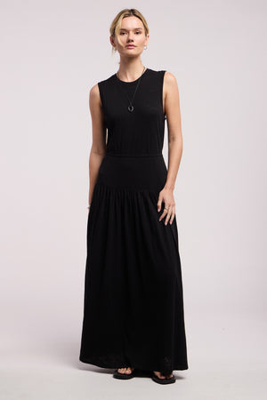 A woman faces forward wearing the LUNETTA DRESS by Velvet by Graham & Spencer, styled with black sandals and a necklace, against a plain light background.