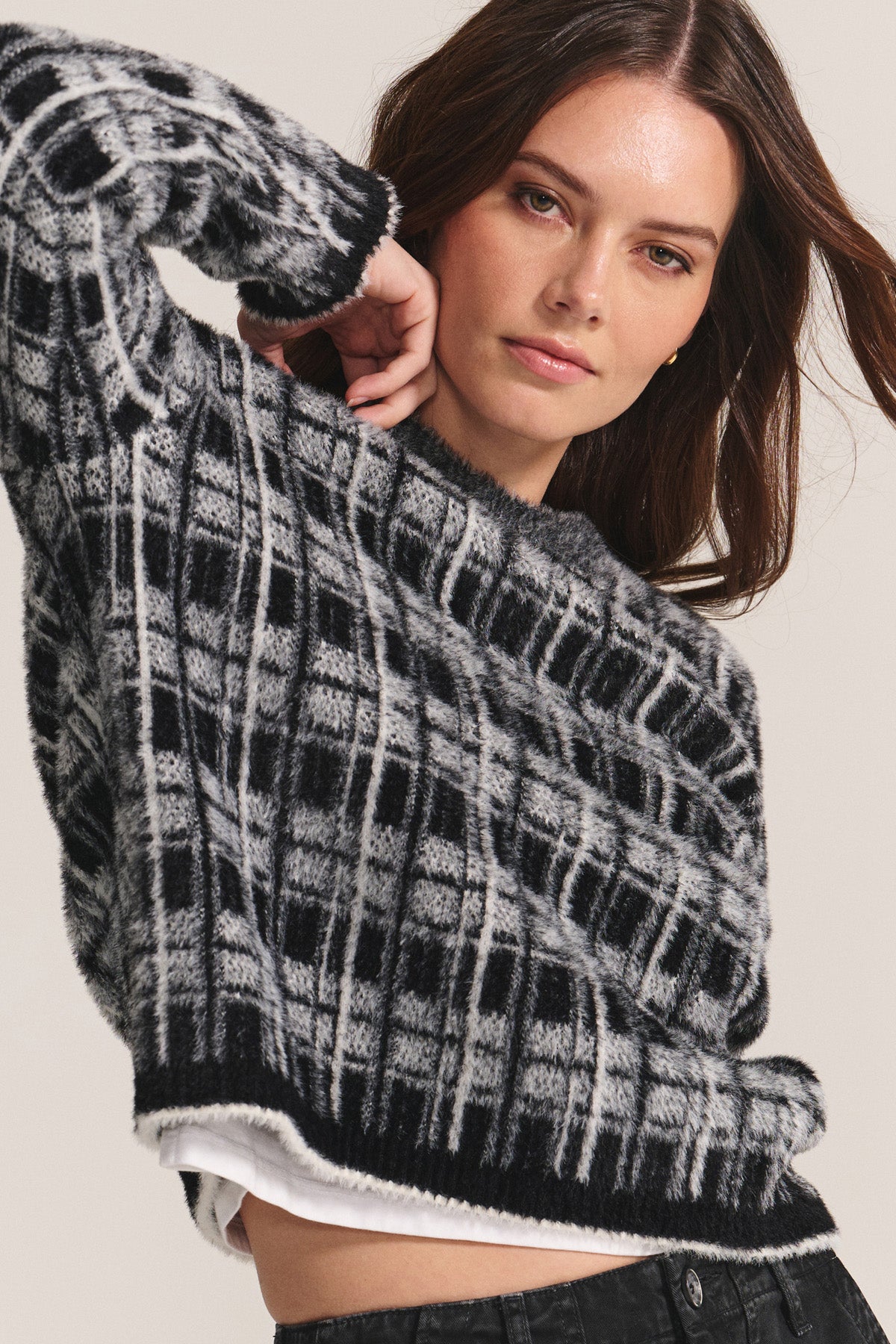 A woman models the LACEY SWEATER by Velvet by Graham & Spencer—a black and gray plaid crewneck—layered over a white shirt with black pants, posing against a neutral background.