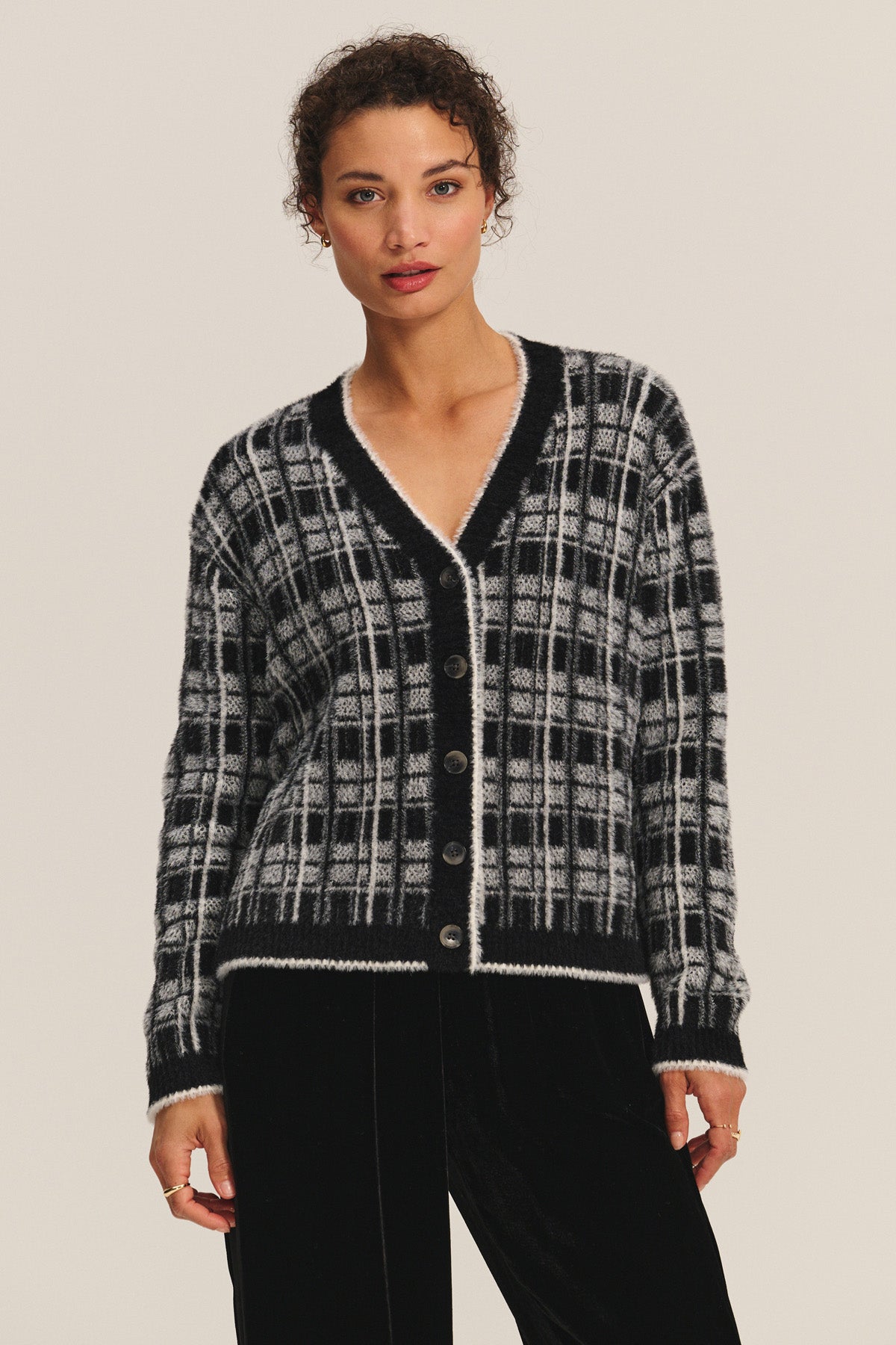 A person wears the WANDA CARDIGAN by Velvet by Graham & Spencer—a black and white plaid V-neck button-up—standing against a plain light background.-40688843161793