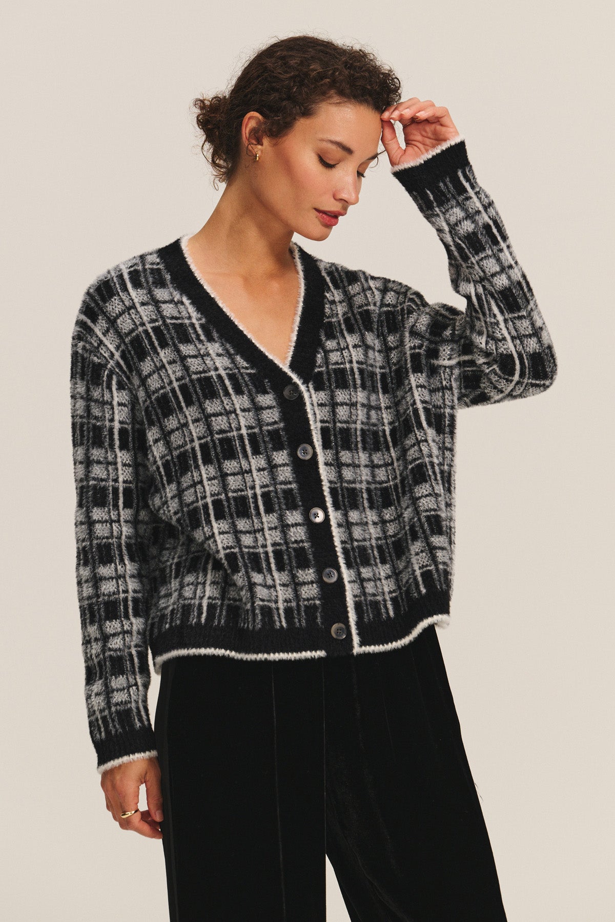 A person wears the WANDA CARDIGAN by Velvet by Graham & Spencer in black and white plaid with black pants, standing against a plain light background.