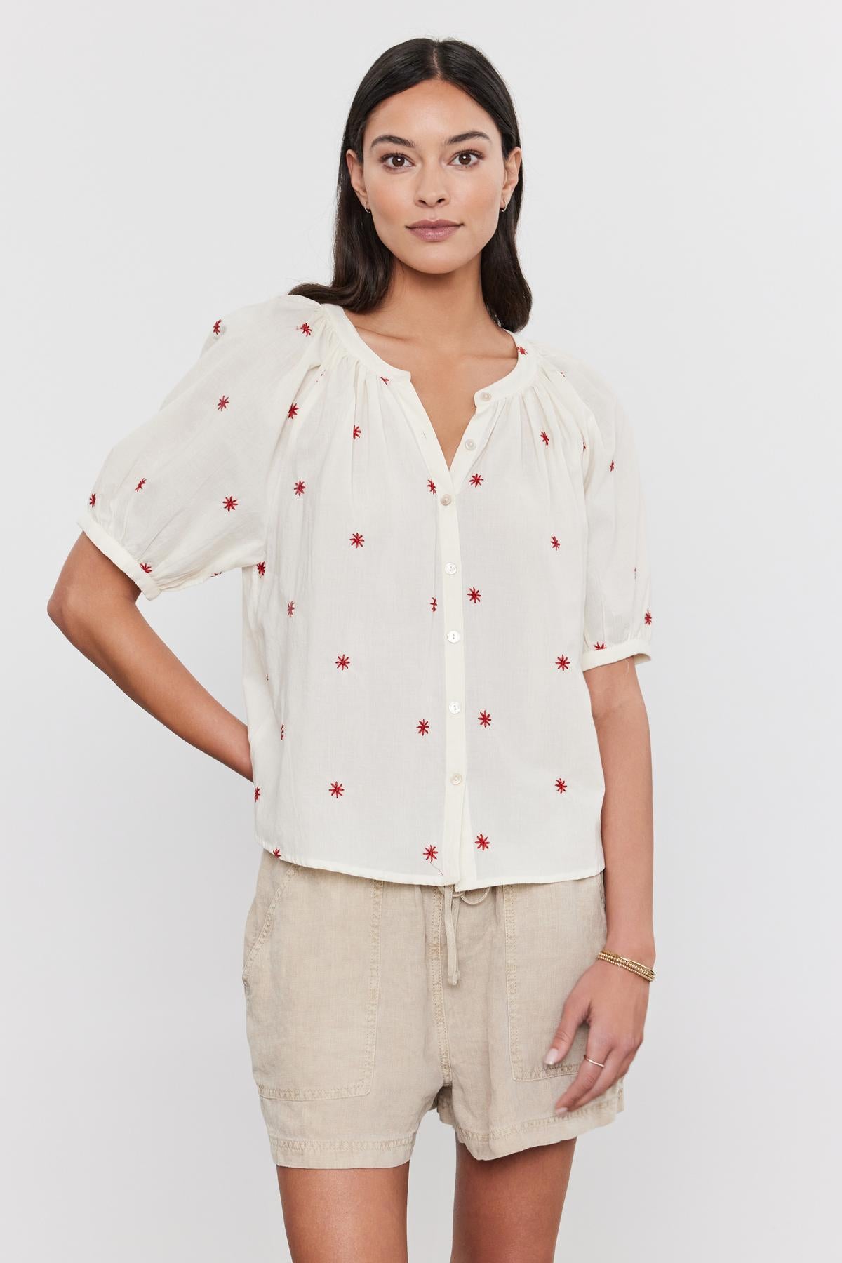 A woman wearing a white AMIRA TOP with red floral embroidery and beige shorts, standing against a plain background. Brand Name: Velvet by Graham & Spencer-36910000341185