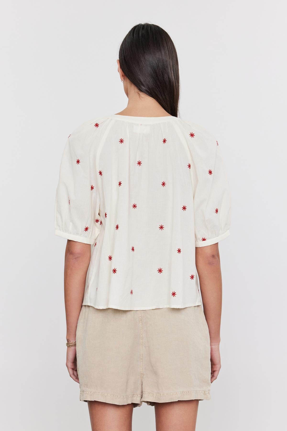 A woman from behind wearing a white Velvet by Graham & Spencer AMIRA TOP with red floral embroidery and button front detail, paired with a beige skirt.-36910000373953