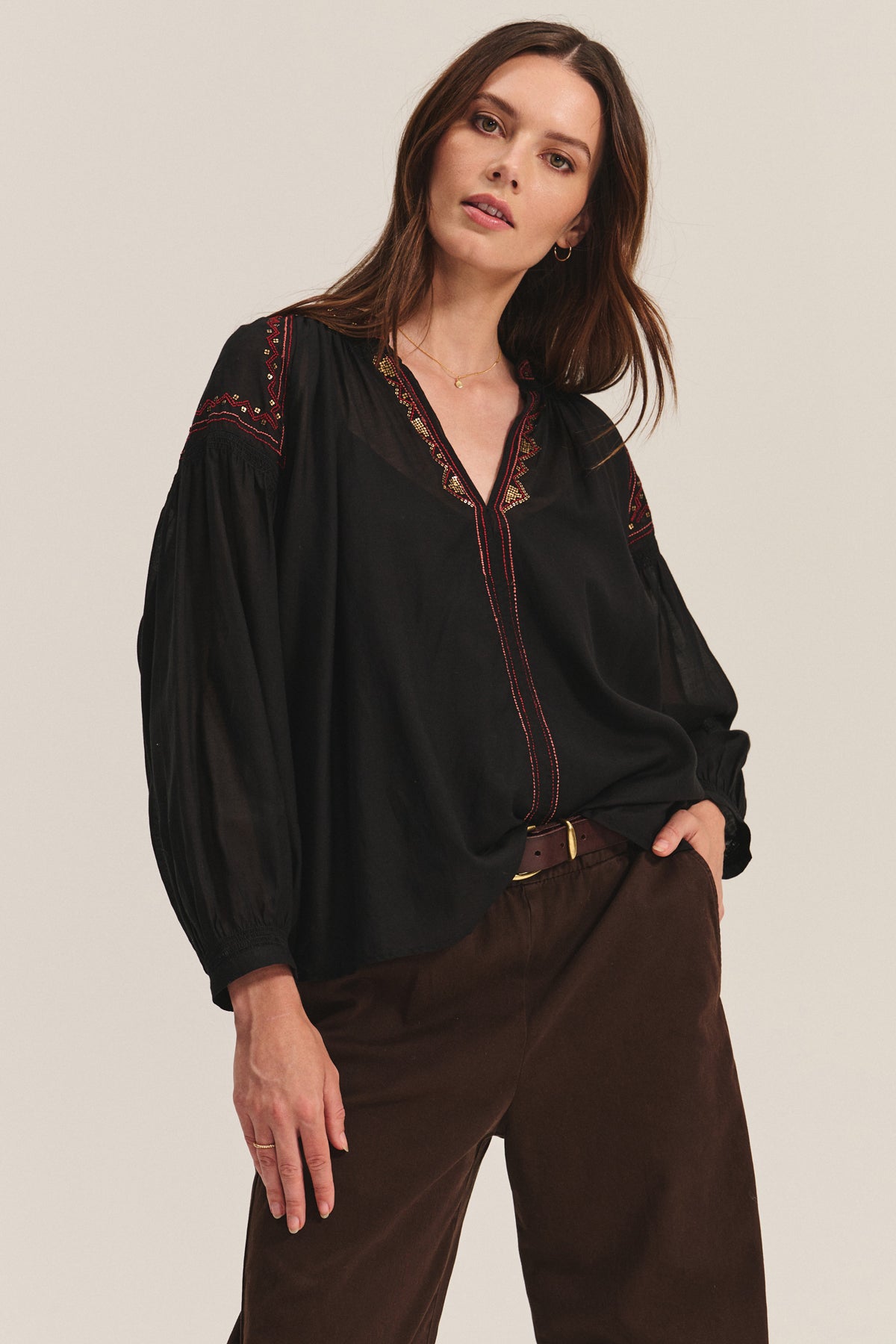 A woman wears the BRIDGET TOP by Velvet by Graham & Spencer—a black cotton voile top with beaded embroidered details—paired with brown pants, looking at the camera against a neutral background.