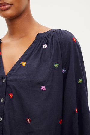 A woman wearing a navy ARETHA EMBROIDERED BOHO TOP by Velvet by Graham & Spencer with embroidered flowers.