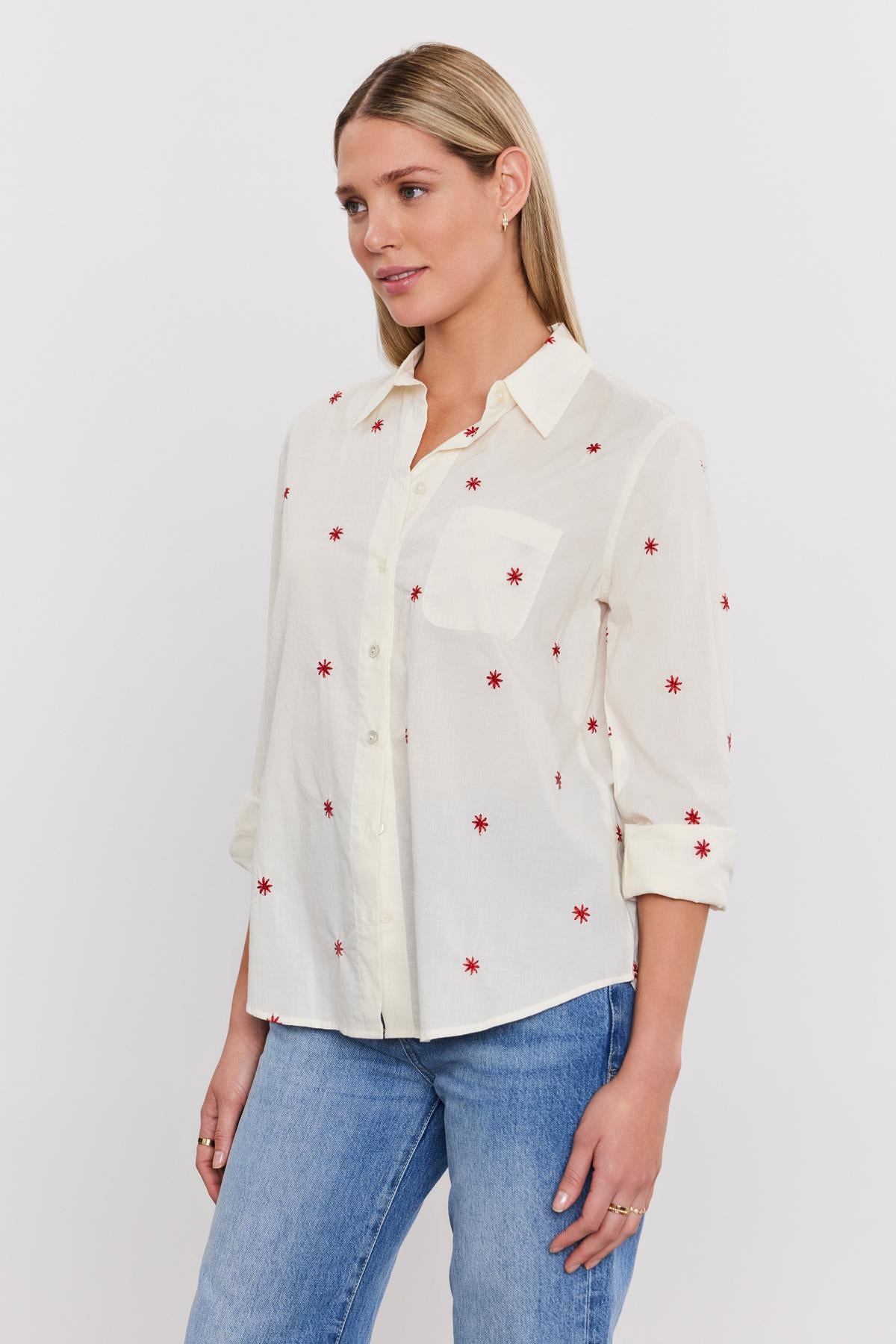   A person in the EMBERLY SHIRT by Velvet by Graham & Spencer, featuring red star patterns, paired with blue jeans, stands against a plain white background. 