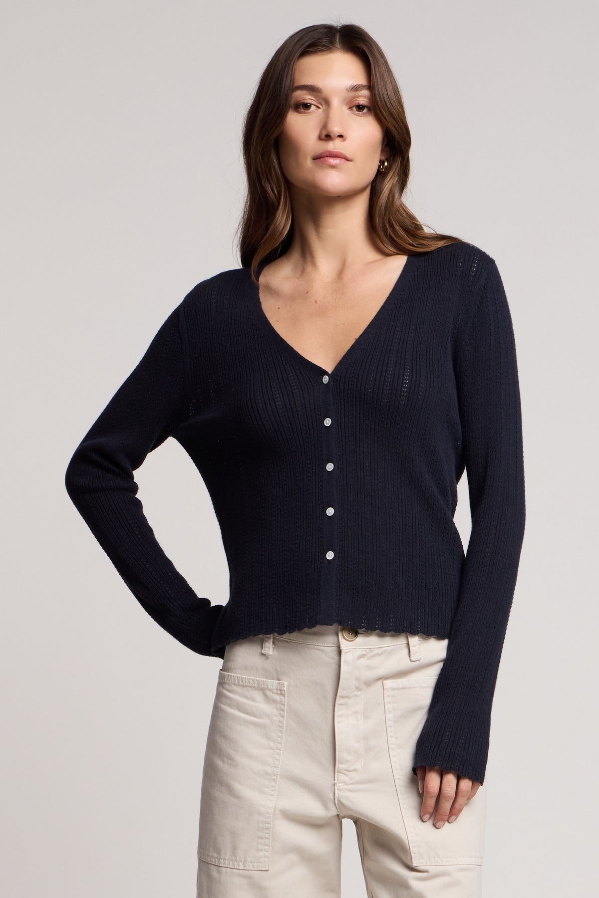 A woman wearing the Velvet by Graham & Spencer OTTILIE CARDIGAN in navy blue and light beige pants stands against a plain background.-41527199236289