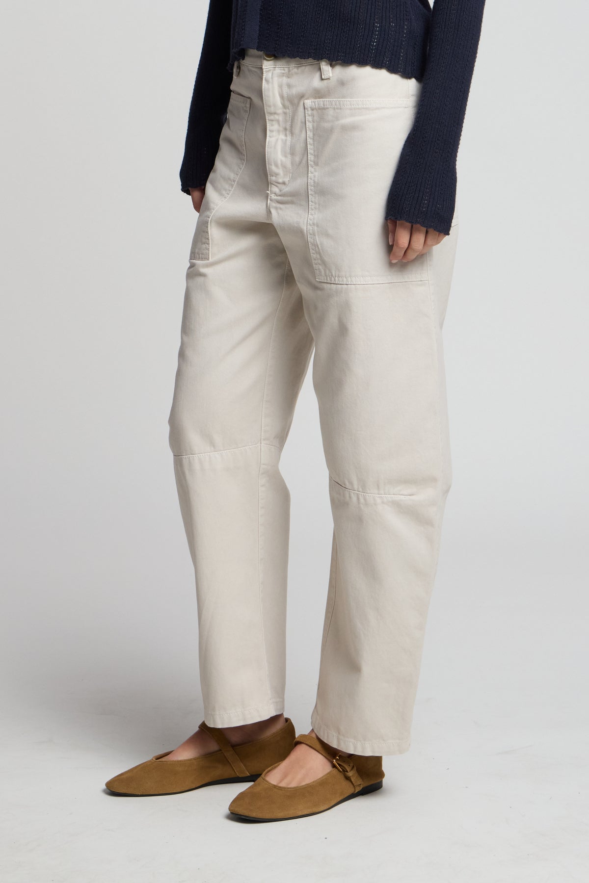 Wearing Velvet by Graham & Spencer’s BRYLIE PANT—off-white cotton twill trousers with utilitarian patch pockets—paired with a dark long-sleeve sweater and brown flats, standing against a plain, light background.