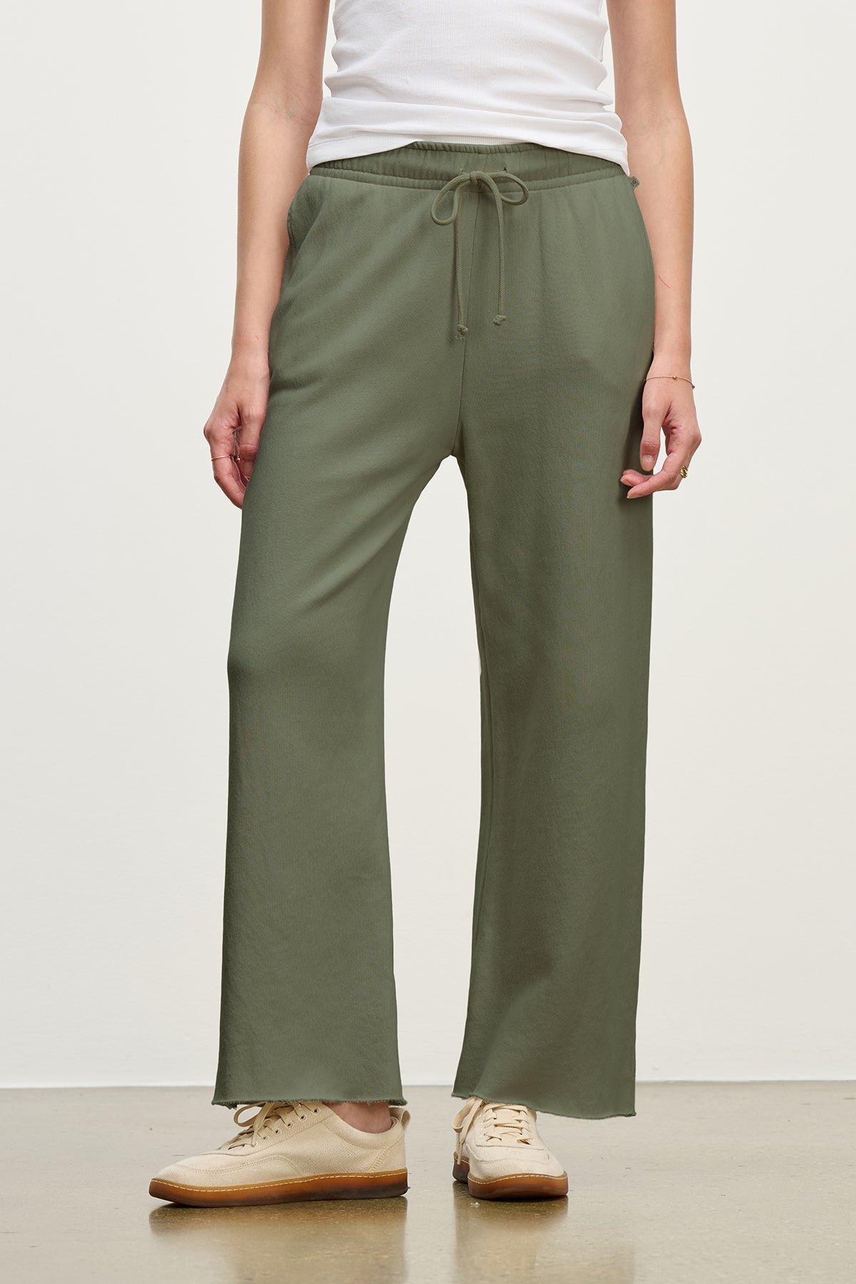 A person in a white top and MONTECITO SWEATPANT by Velvet by Jenny Graham, featuring olive green flared legs in organic cotton with a drawstring, paired with beige shoes, stands against a plain background.-38754052178113