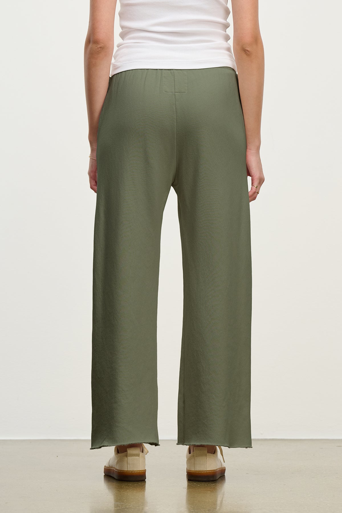 A person wearing Velvet by Jenny Graham's "MONTECITO SWEATPANT" in olive green, paired with a white sleeveless top and beige shoes, stands on a light-colored floor.-38754052243649