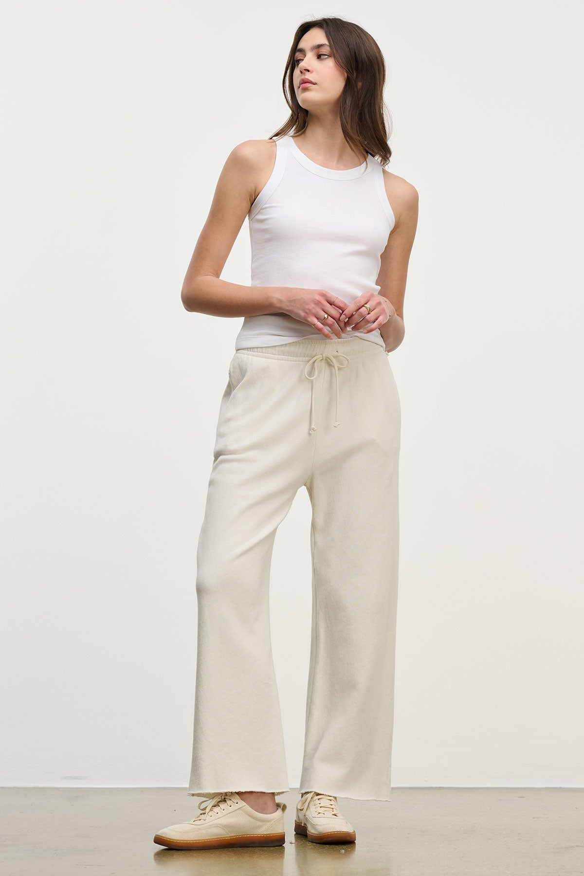   Person standing against a plain background, wearing the CRUZ TANK TOP in white ribbed cotton-modal by Velvet by Jenny Graham, paired with light beige drawstring pants and beige shoes—a perfect addition to any capsule wardrobe. 