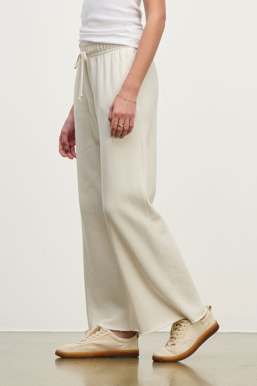 Someone wearing MONTECITO SWEATPANT by Velvet by Jenny Graham and beige sneakers stands against a plain background.