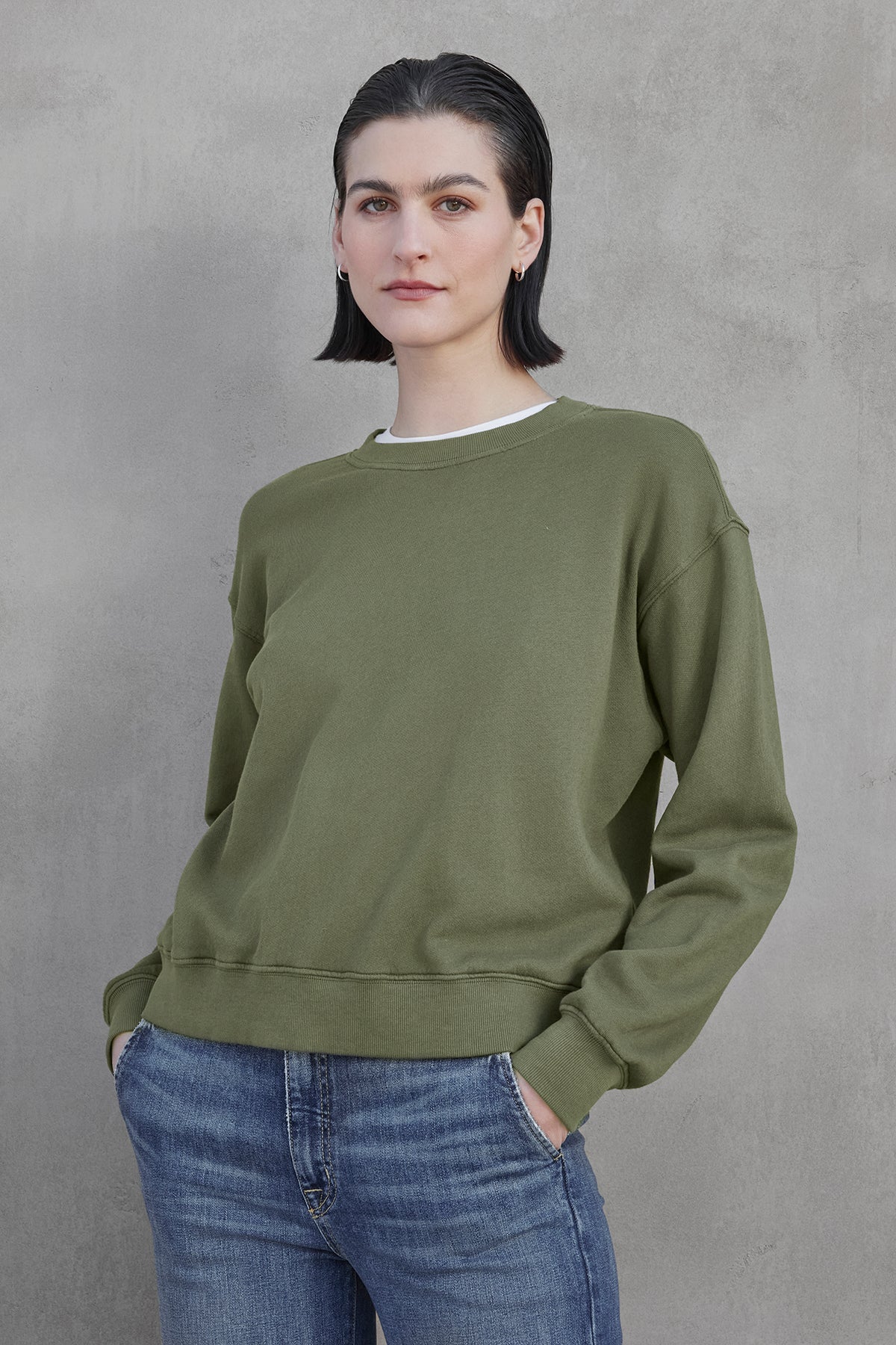   A person stands against a gray background wearing the YNEZ SWEATSHIRT from Velvet by Jenny Graham, made of organic cotton, paired with jeans. 