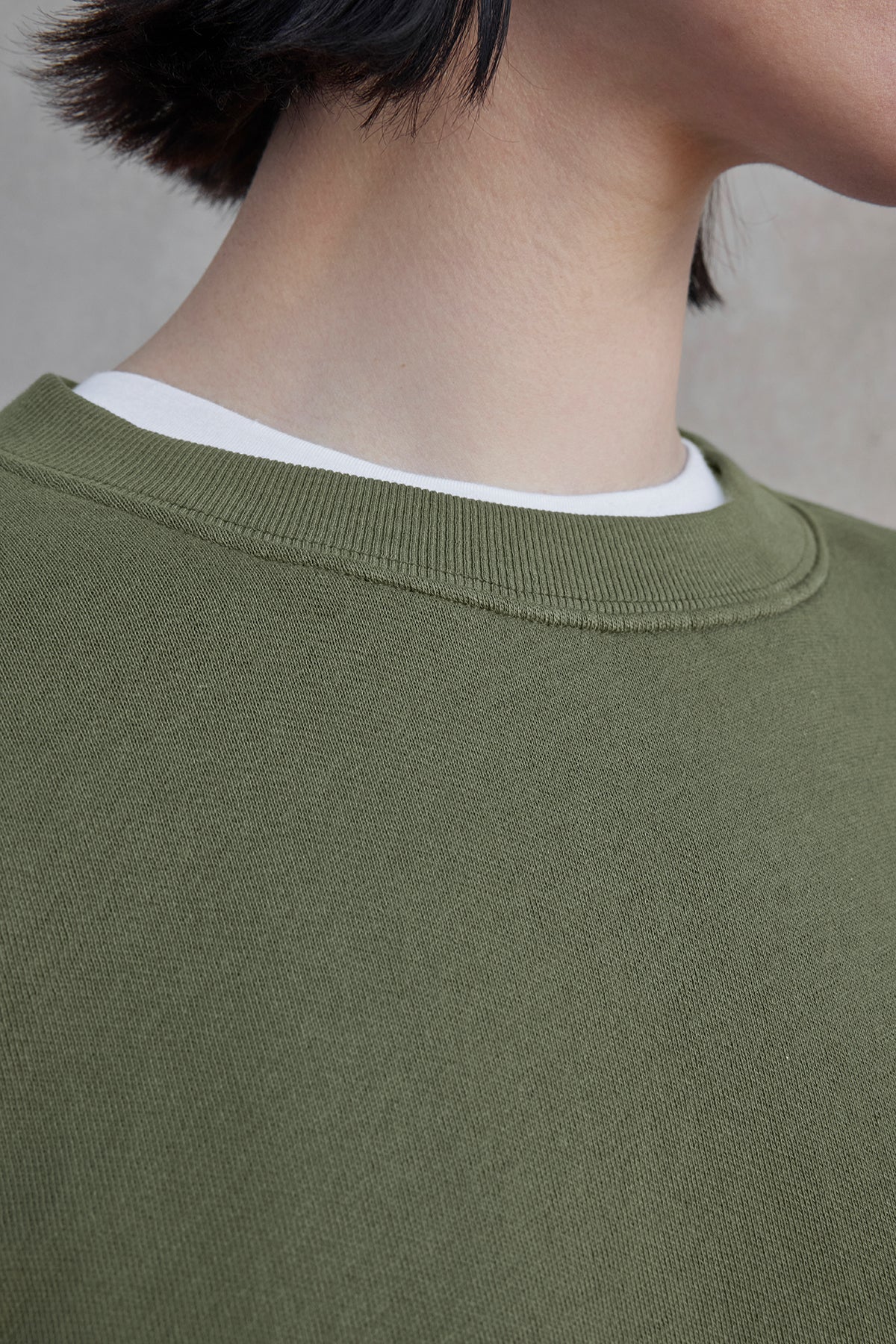   Close-up of a person wearing the YNEZ SWEATSHIRT by Velvet by Jenny Graham, a green crew-neck made from organic cotton, layered over a crisp white shirt. 