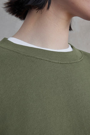 Close-up of a person wearing the YNEZ SWEATSHIRT by Velvet by Jenny Graham, a green crew-neck made from organic cotton, layered over a crisp white shirt.