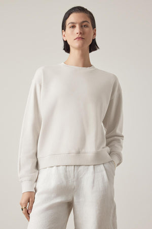 Person wearing a Velvet by Jenny Graham YNEZ SWEATSHIRT made of organic cotton and white pants, standing against a plain background with a neutral expression.