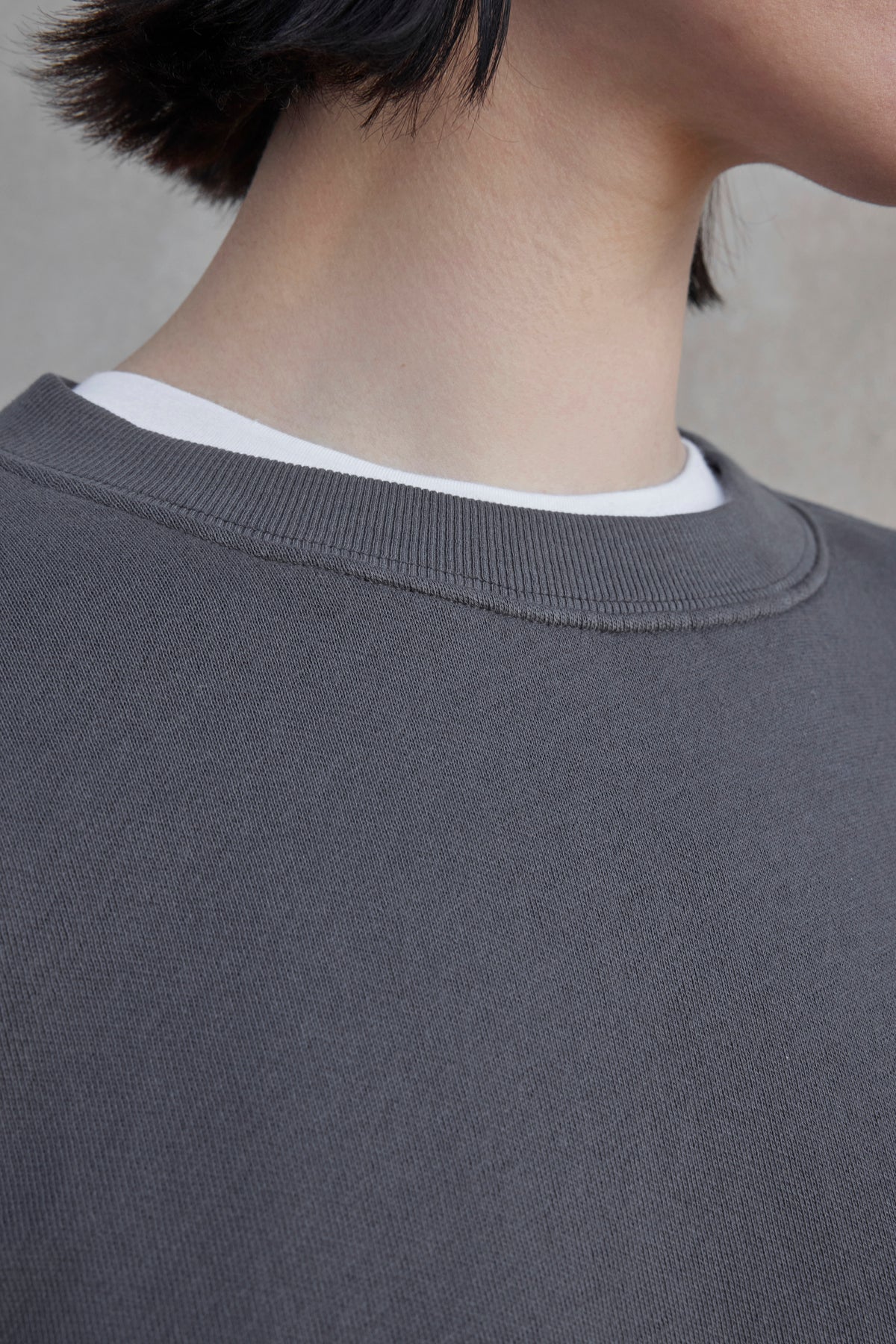 Close-up of a person's neck and shoulders wearing a white t-shirt under the Velvet by Jenny Graham YNEZ sweatshirt, a gray crewneck made from organic cotton.-37659922530497