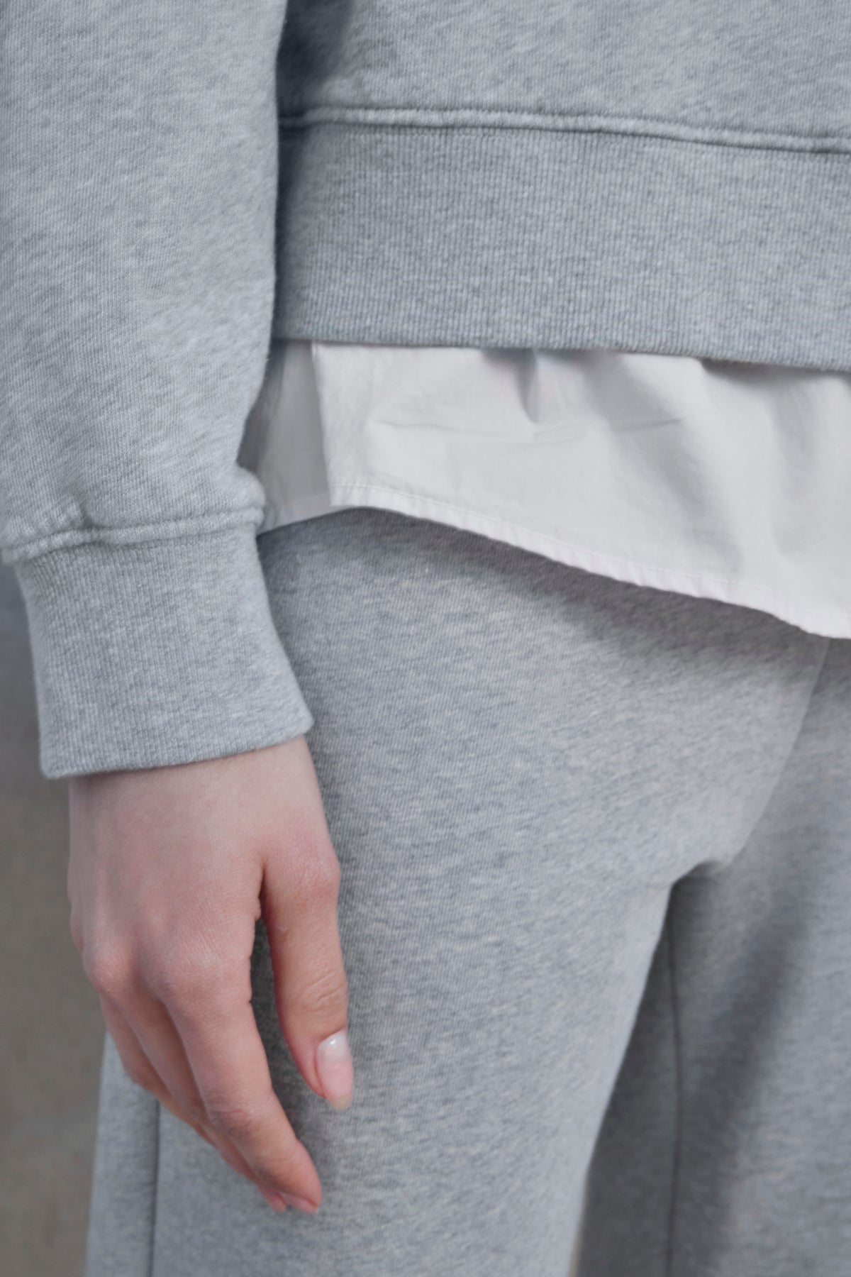   Close-up of a person wearing the YNEZ SWEATSHIRT by Velvet by Jenny Graham, paired with matching light gray sweatpants made from organic cotton. A white shirt peeks out from underneath the sweatshirt, with only the lower torso and one hand visible. 