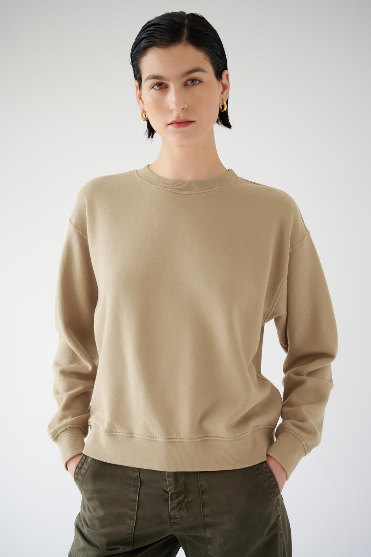 Woman posing in a plain beige Velvet by Jenny Graham Ynez sweatshirt and green pants against a light background.-36463630745793